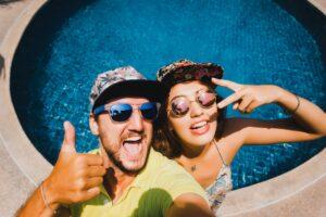 Paar mit Sonnenbrillen macht Selfie vor ihrem Pool